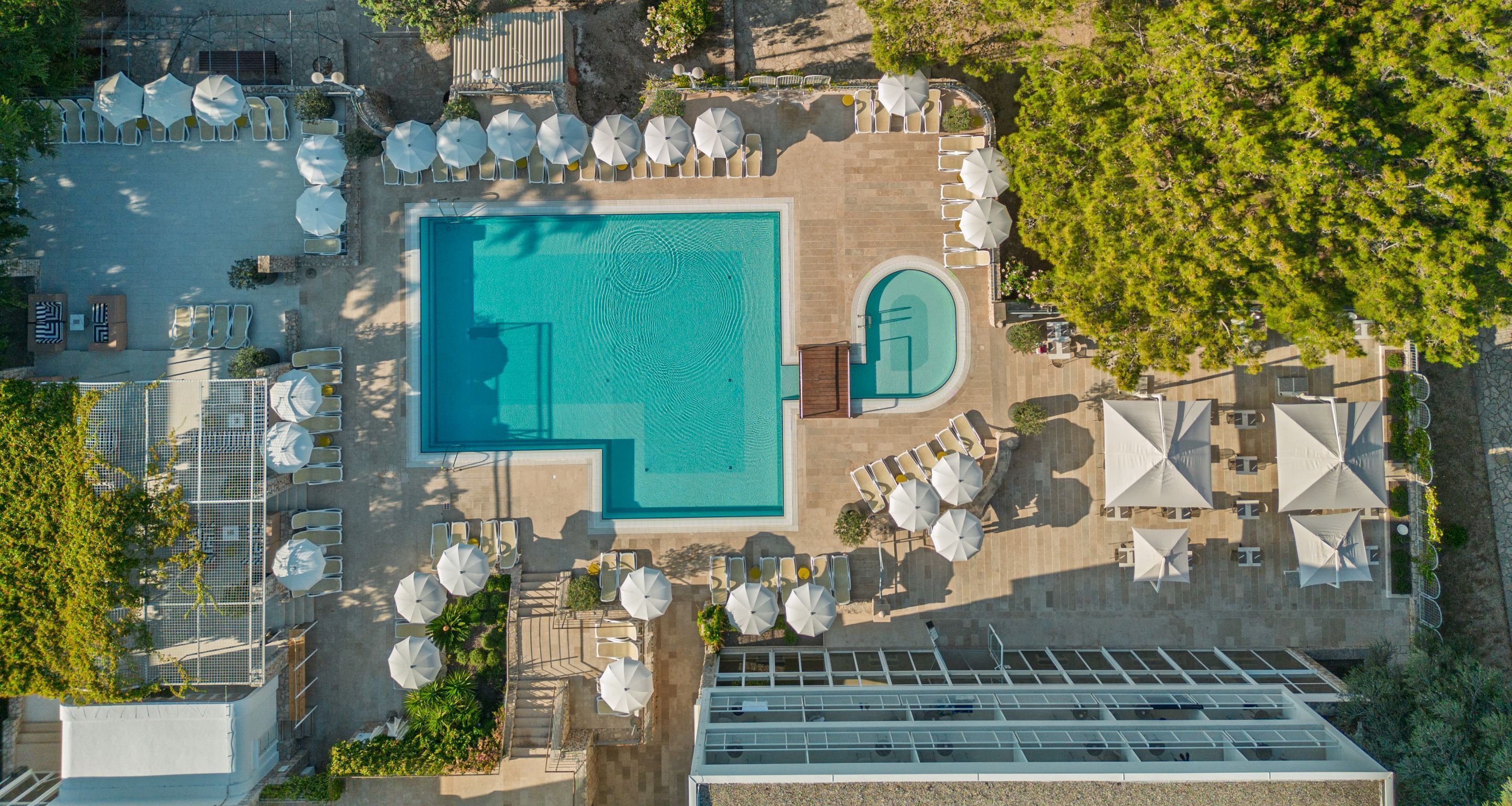 An aerial view of a resort with a central swimming pool, sun loungers, and umbrellas.