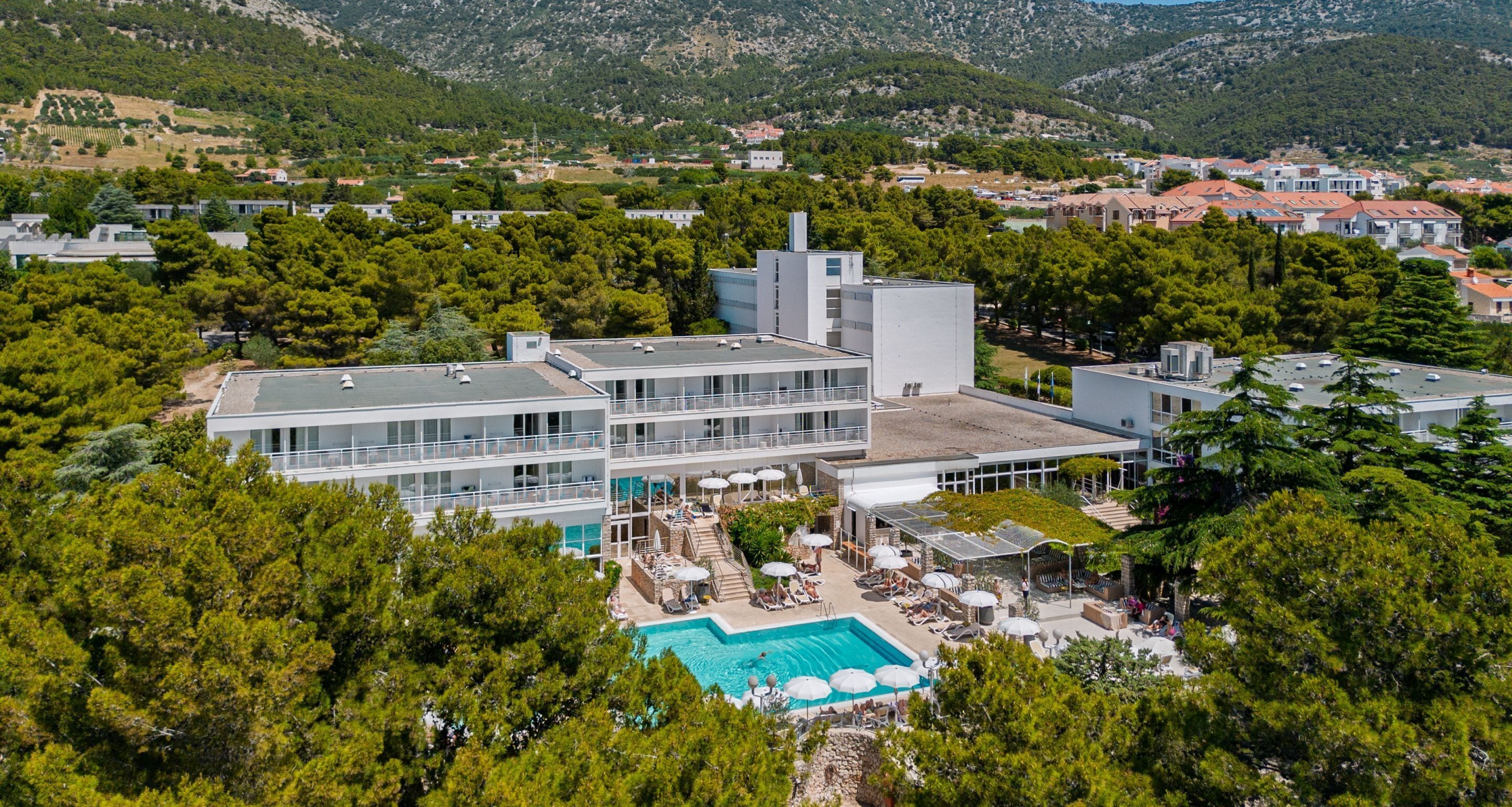 A modern hotel with a rooftop pool, surrounded by lush greenery and a mountainous backdrop.