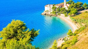 A coastal building with a tower, surrounded by clear blue waters and green trees. - Bluesun Hotel Borak (Bol)