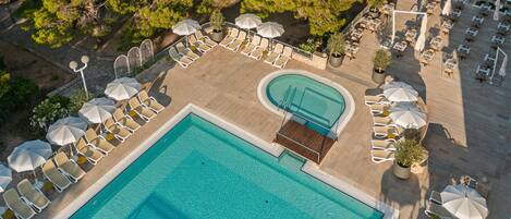 Vue aérienne d’un complexe hôtelier doté d’une piscine centrale, de chaises longues et de parasols.