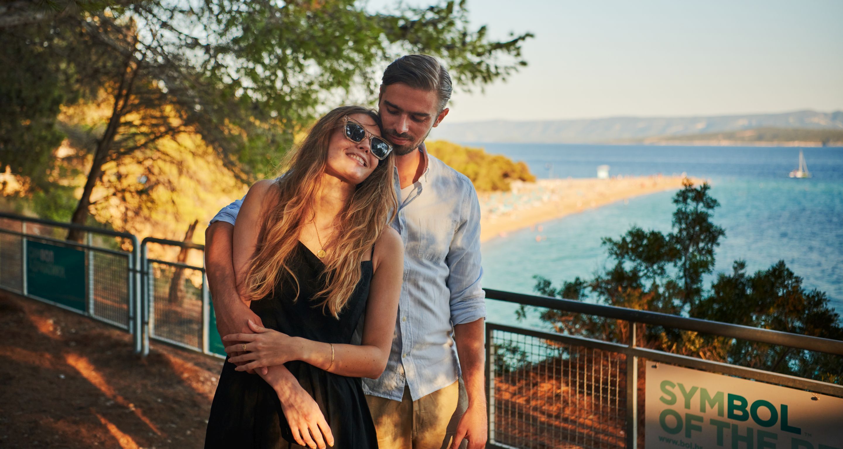 Un couple se tient près d’une balustrade, surplombant une plage, et un panneau indique : « Symbole de la mer ».