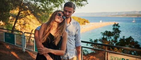 Un couple se tient près d’une balustrade, surplombant une plage, et un panneau indique : « Symbole de la mer ».