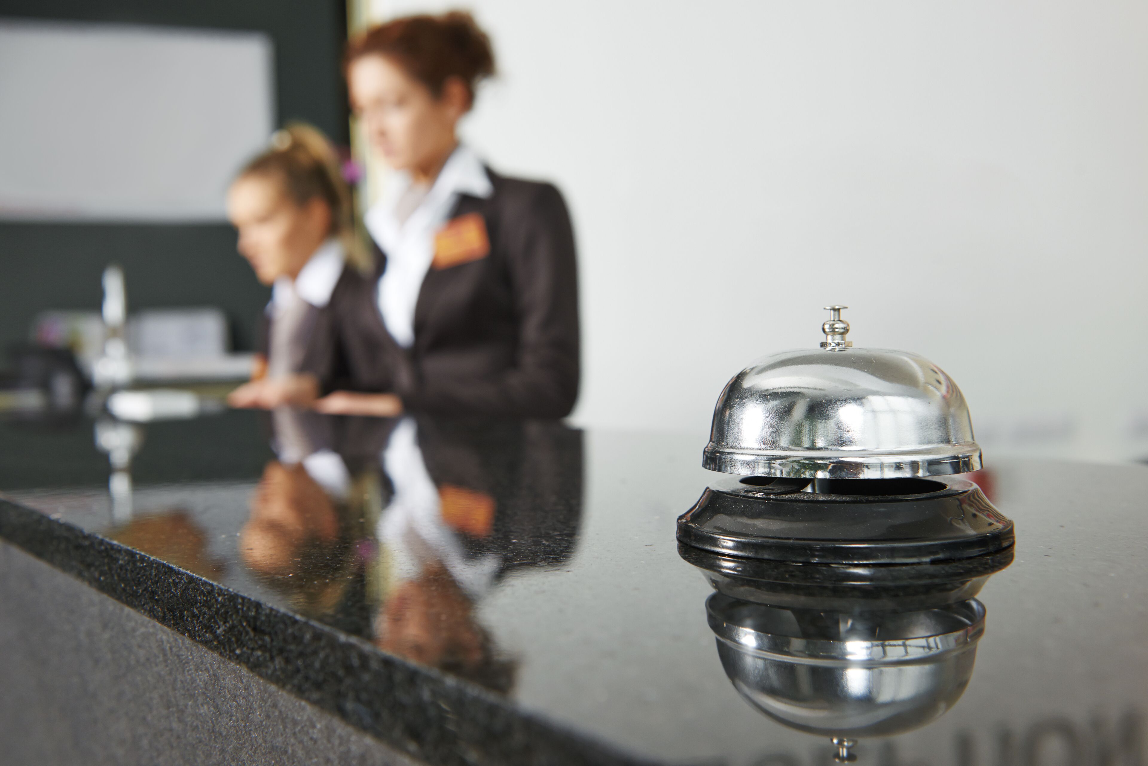 A hotel reception area with a reflective black counter and a silver bell.