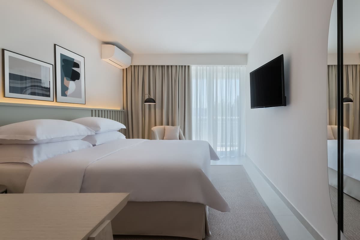 Ein Hotelzimmer mit zwei Betten, einem Flachbildfernseher, einem Sessel und einem großen Spiegel.