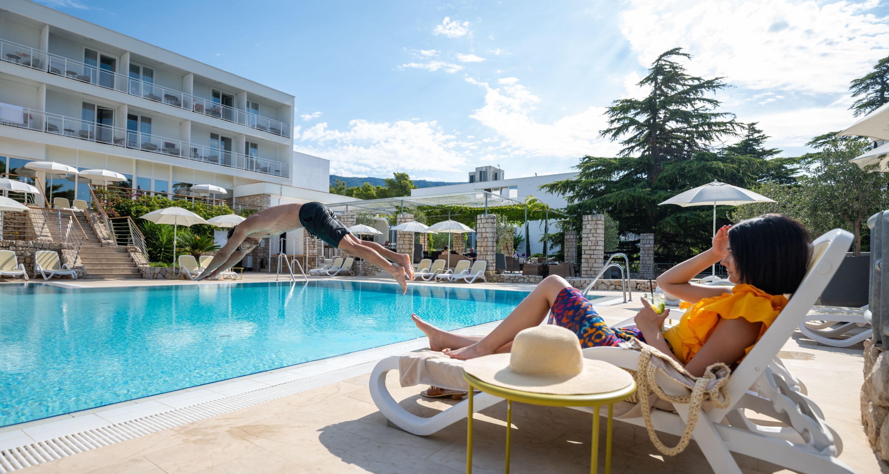 A pool area with lounge chairs and umbrellas, a staircase leading to a building, and a clear sky.