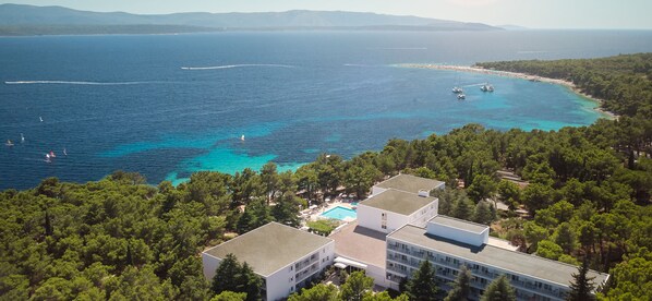 An aerial view of a coastal hotel with multiple buildings, a swimming pool, and a beach area with boats. - Bluesun Hotel Borak (Bol)