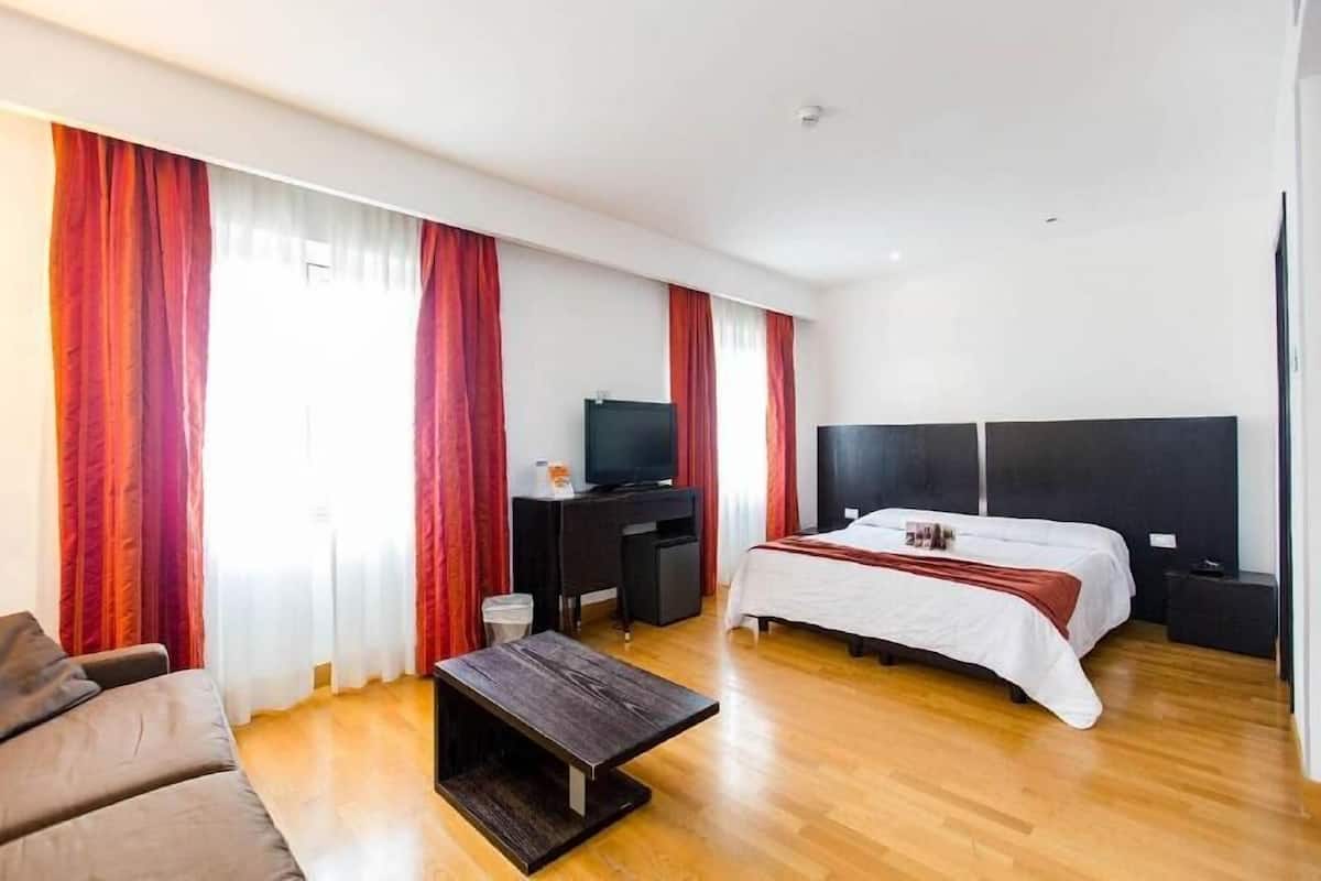 A hotel room with a bed, a desk with a television, a sofa, and a coffee table.
