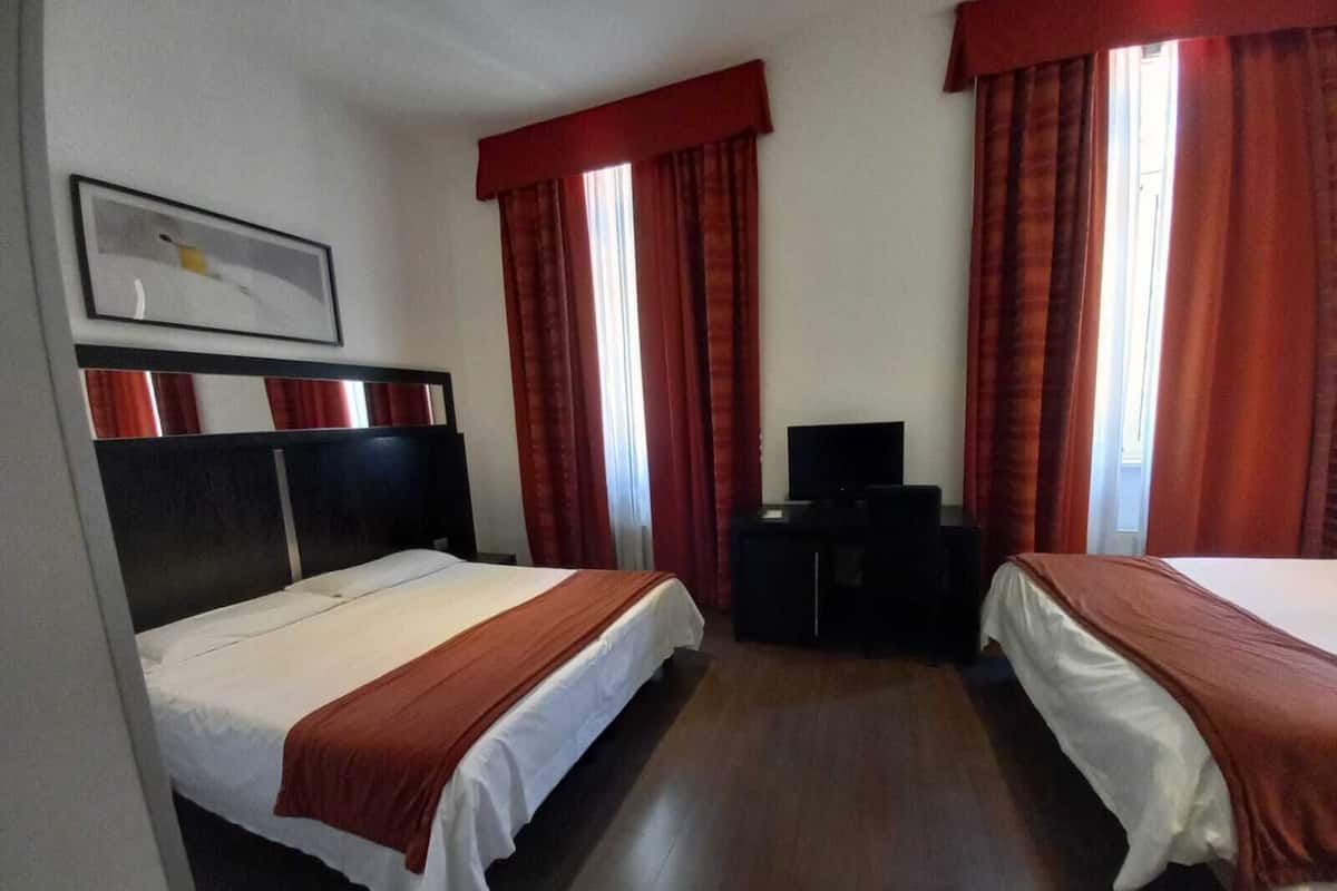 A hotel room with two beds, a TV, and a desk.