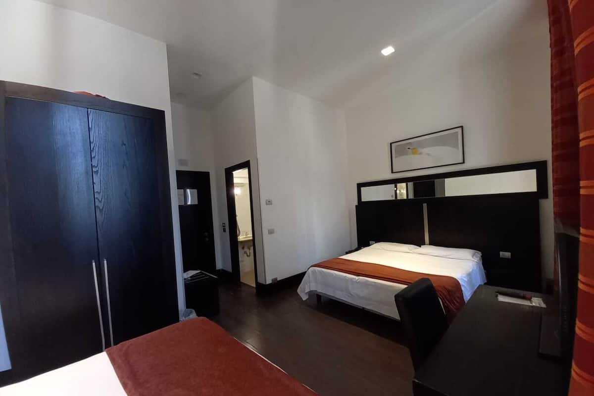 A hotel room with a bed, a desk, a wardrobe, and a bathroom visible through an open door.