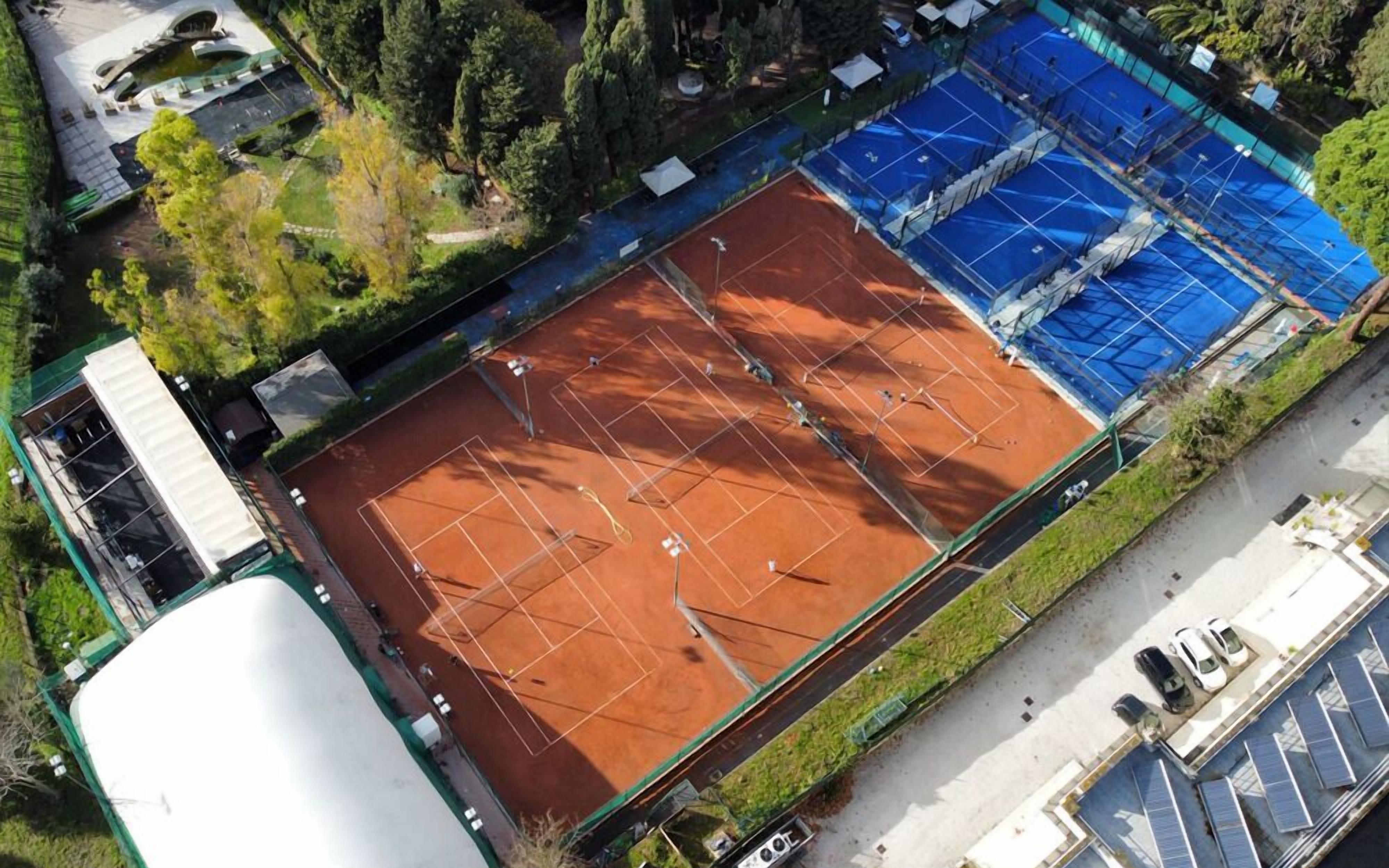 An aerial view of a tennis court with surrounding buildings and greenery.