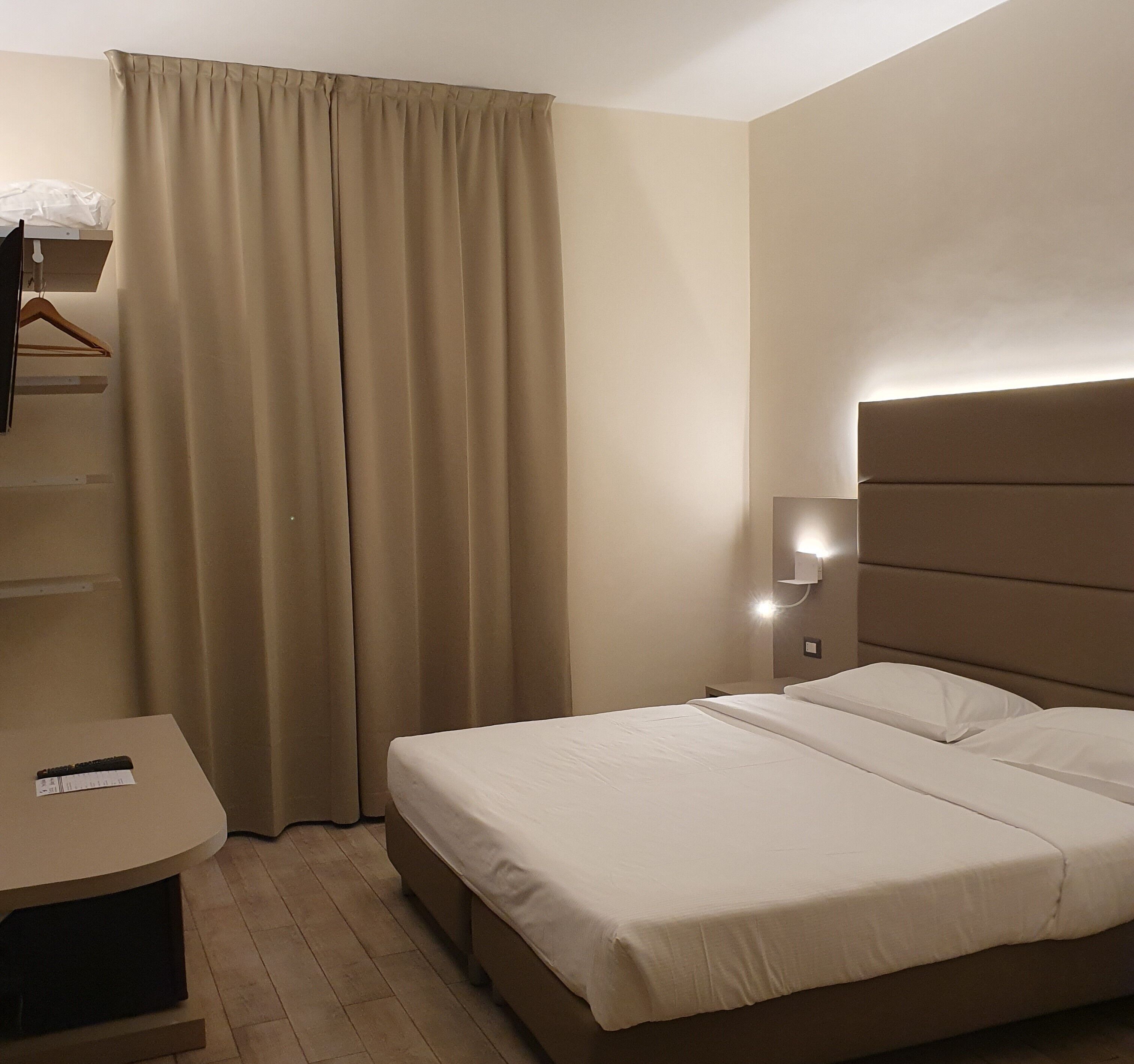 Habitació d'hotel amb llit, una tauleta de nit, una làmpada penjant i un armari.