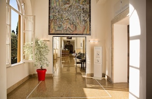 A hallway with a large abstract painting, a red potted plant, and a sign for meeting rooms.