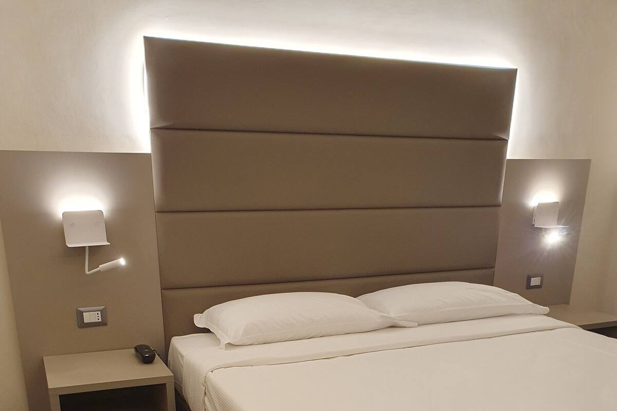 A hotel room with a large bed, two bedside tables, and wall-mounted lighting.