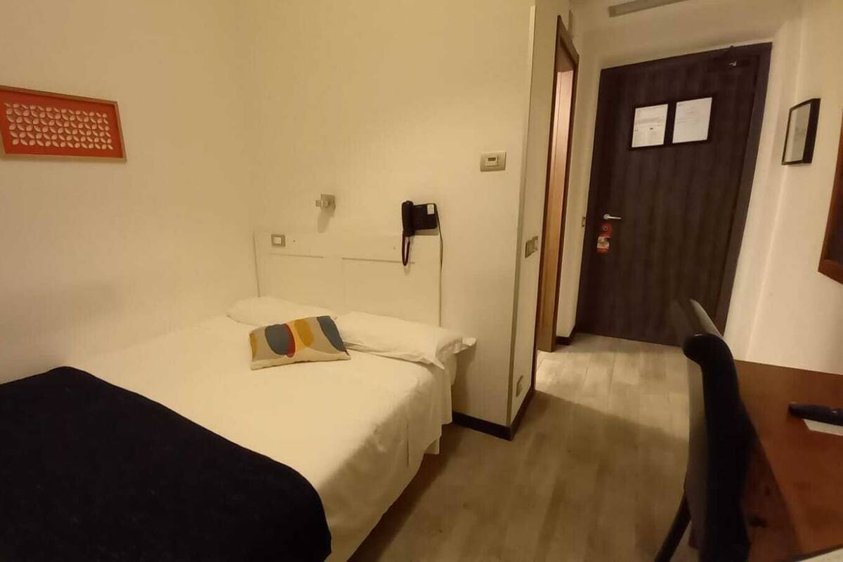A hotel room with a bed, a desk, a chair, and a door.