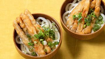 Two bowls of ramen with noodles, a protein, and garnishes on a yellow surface.