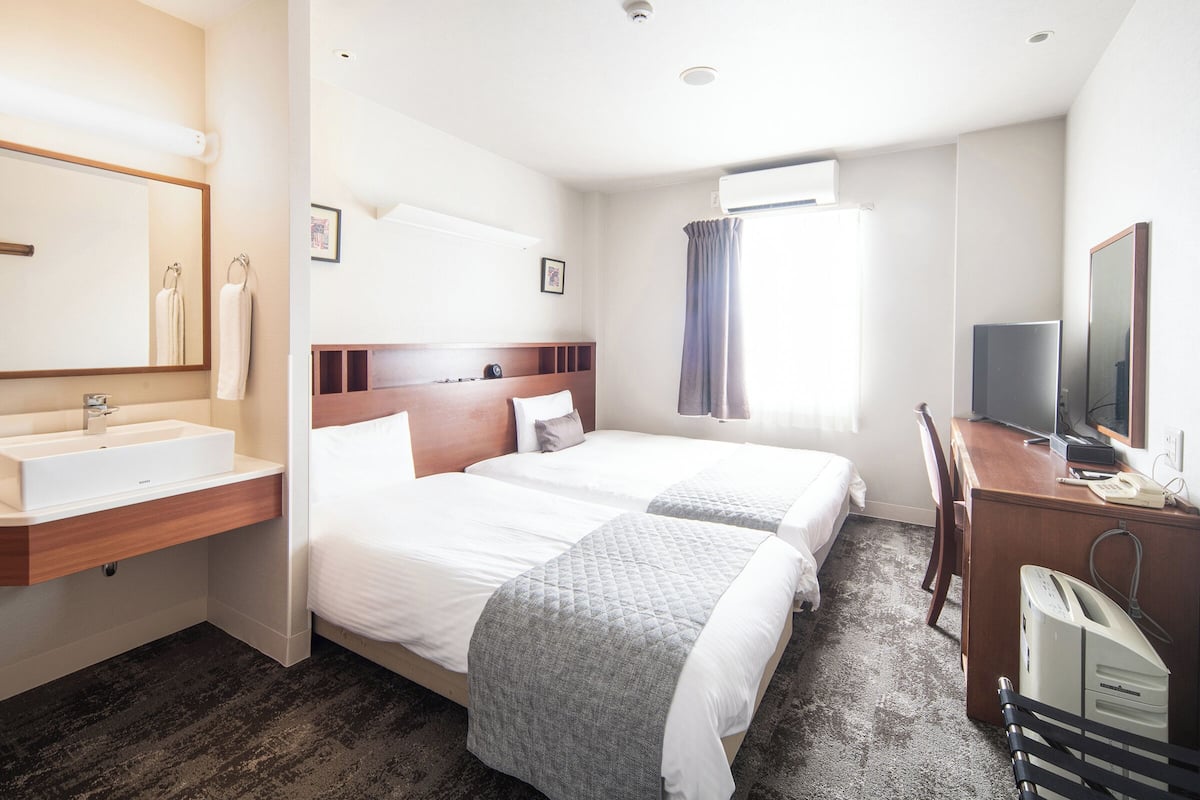 Ein Hotelzimmer mit Bett, Nachttisch, Fernseher und einem Badezimmer mit Waschbecken und Spiegel.