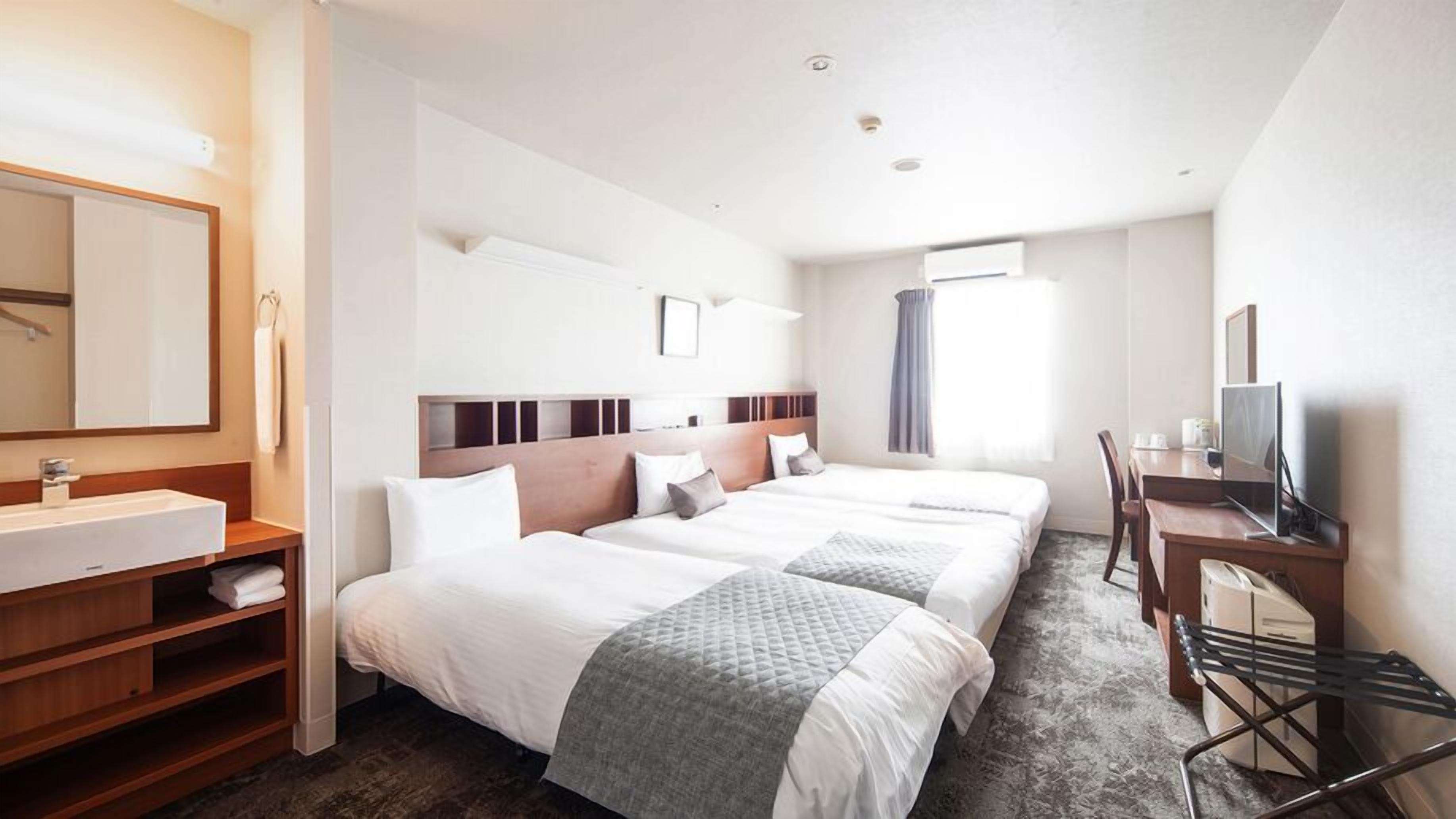 A hotel room with two beds, a desk with a computer, a bathroom with a sink, and a large mirror.