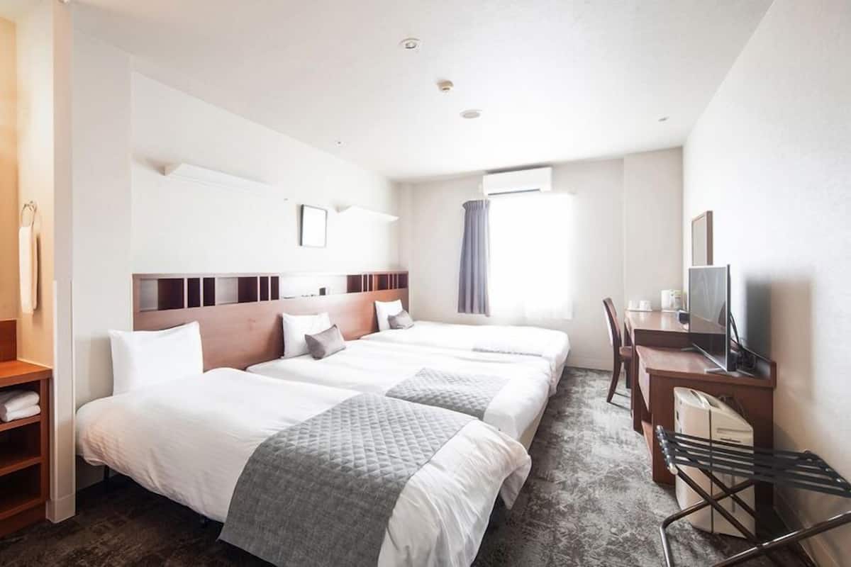 Ein Hotelzimmer mit zwei Betten, einem Schreibtisch mit Computer, einem Badezimmer mit Waschbecken und einem großen Spiegel.
