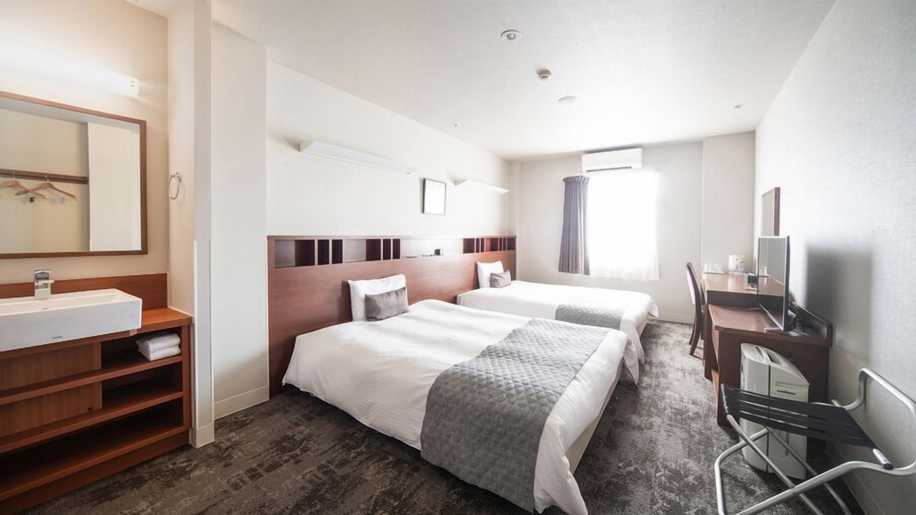 A hotel room with a large bed, a desk, a chair, a TV, a mirror, and a bathroom with a sink and shelves.