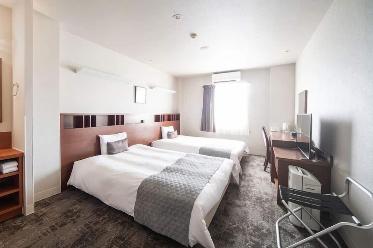 Ein Hotelzimmer mit einem großen Bett, einem Schreibtisch, einem Sessel, einem Fernseher, einem Spiegel und einem Badezimmer mit Waschbecken und Ablagen.