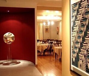 A dining area with tables and chairs, a red wall, and a painting.