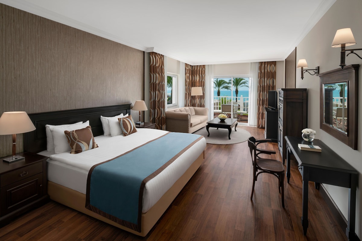 Habitació d'hotel amb un llit gran, un sofà, una taula de treball i vistes a l'oceà.