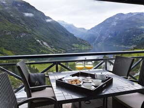 Una mesa de comedor con alimentos para el desayuno y vasos de jugo de naranja, con vistas a un paisaje montañoso y un lago.
