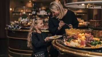 En buffetopstilling med forskellige retter, og en person serverer mad til en anden.