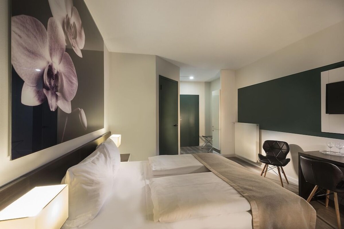 Una habitación de hotel con cama, escritorio, silla, espejo grande y televisión montada en la pared.