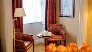 A hotel room with two leather armchairs, a small round table with a tray of breakfast items, and a framed picture of the Eiffel Tower on the wall. - Grange Buckingham (London)