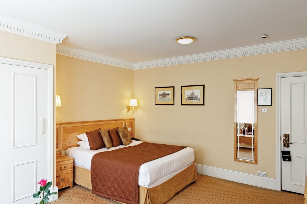 A hotel room with a large bed, a wooden headboard, two wall-mounted lamps, and a mirror.