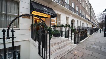 The Clarendon Hotel with a black awning, stone steps, and a black wrought iron fence.
