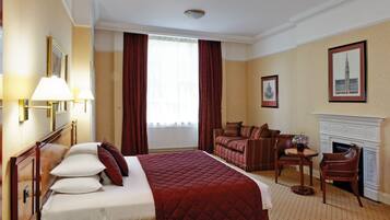 A hotel room with a large bed, a sitting area with a fireplace, and a view of a building through the window.