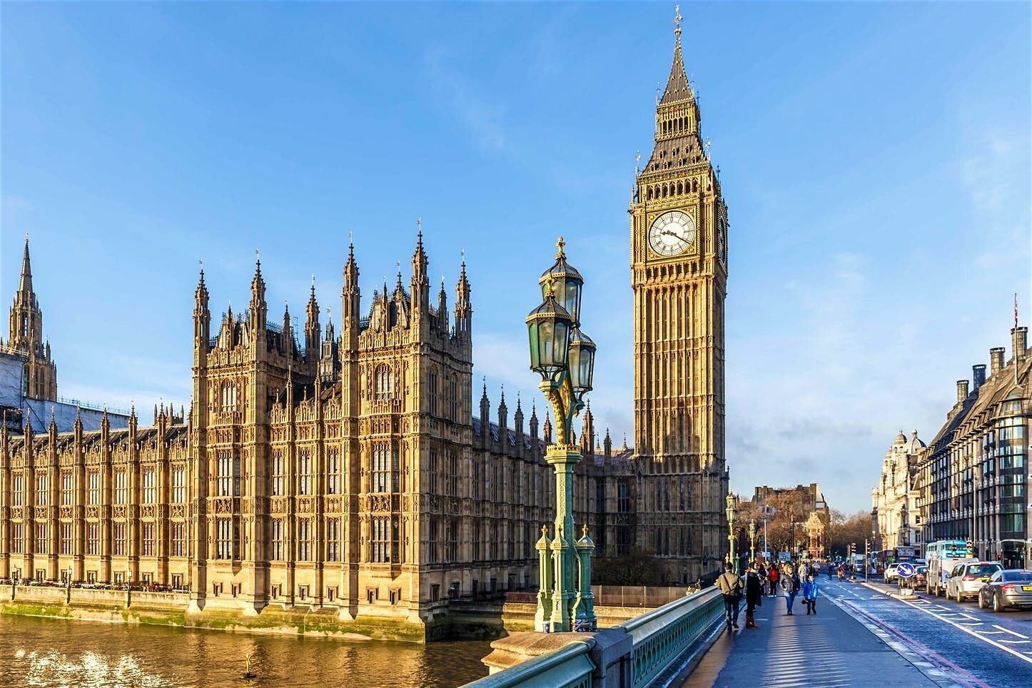 A historic building with intricate architecture, a prominent clock tower, and a river in the foreground.