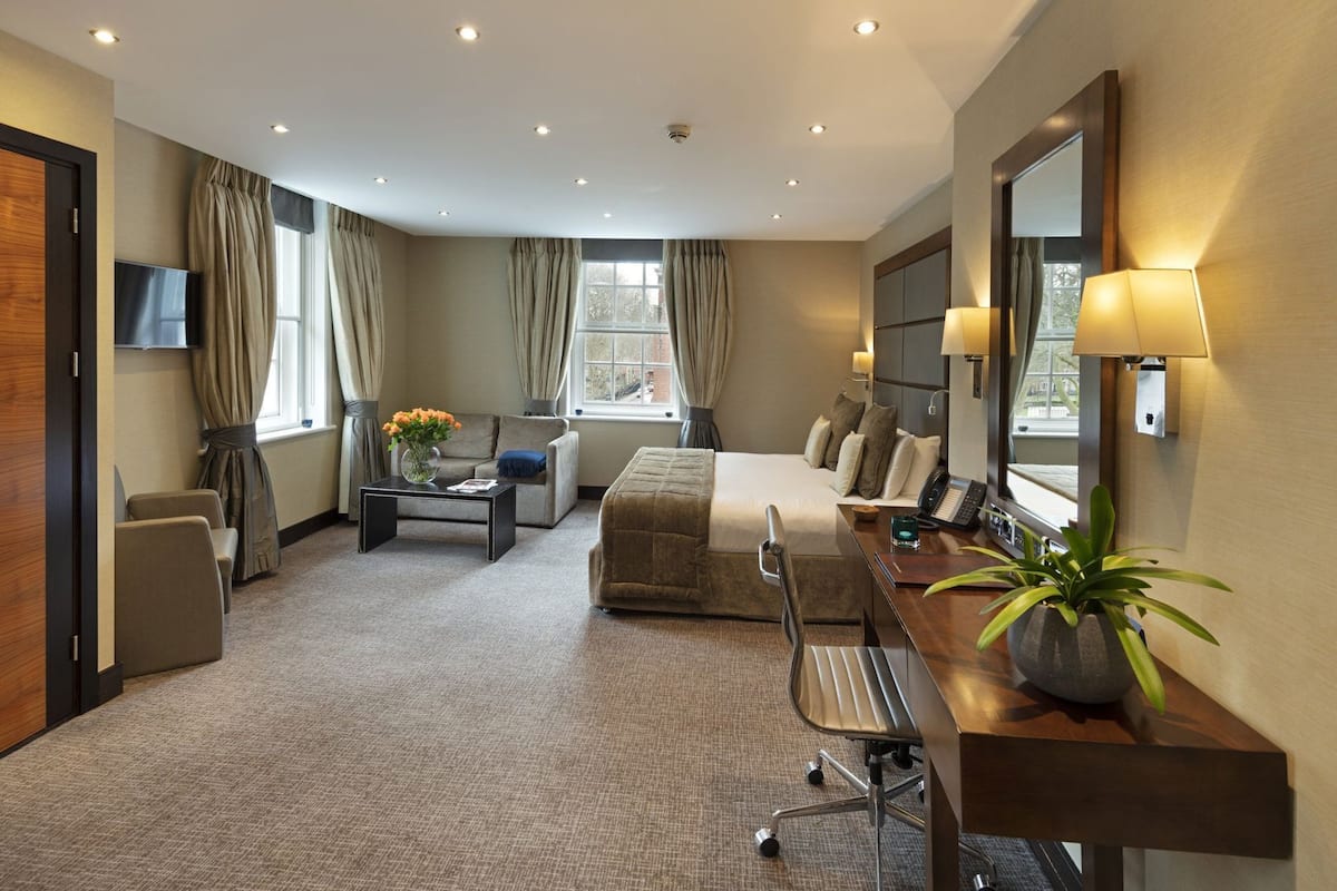 Habitación de hotel con cama, escritorio, silla, sofá, televisión y ventana con cortinas.