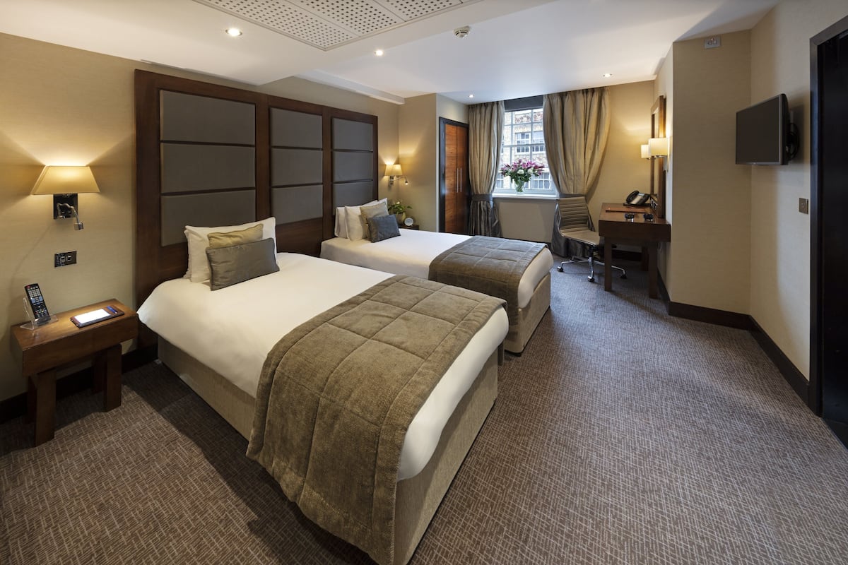 Habitación de hotel con dos camas, un escritorio con silla, televisión y ventana con cortinas.