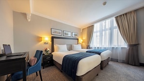 A hotel room with two beds, a desk with a laptop, a chair, and a nightstand with a lamp. - Wellington Hotel by Blue Orchid (London)