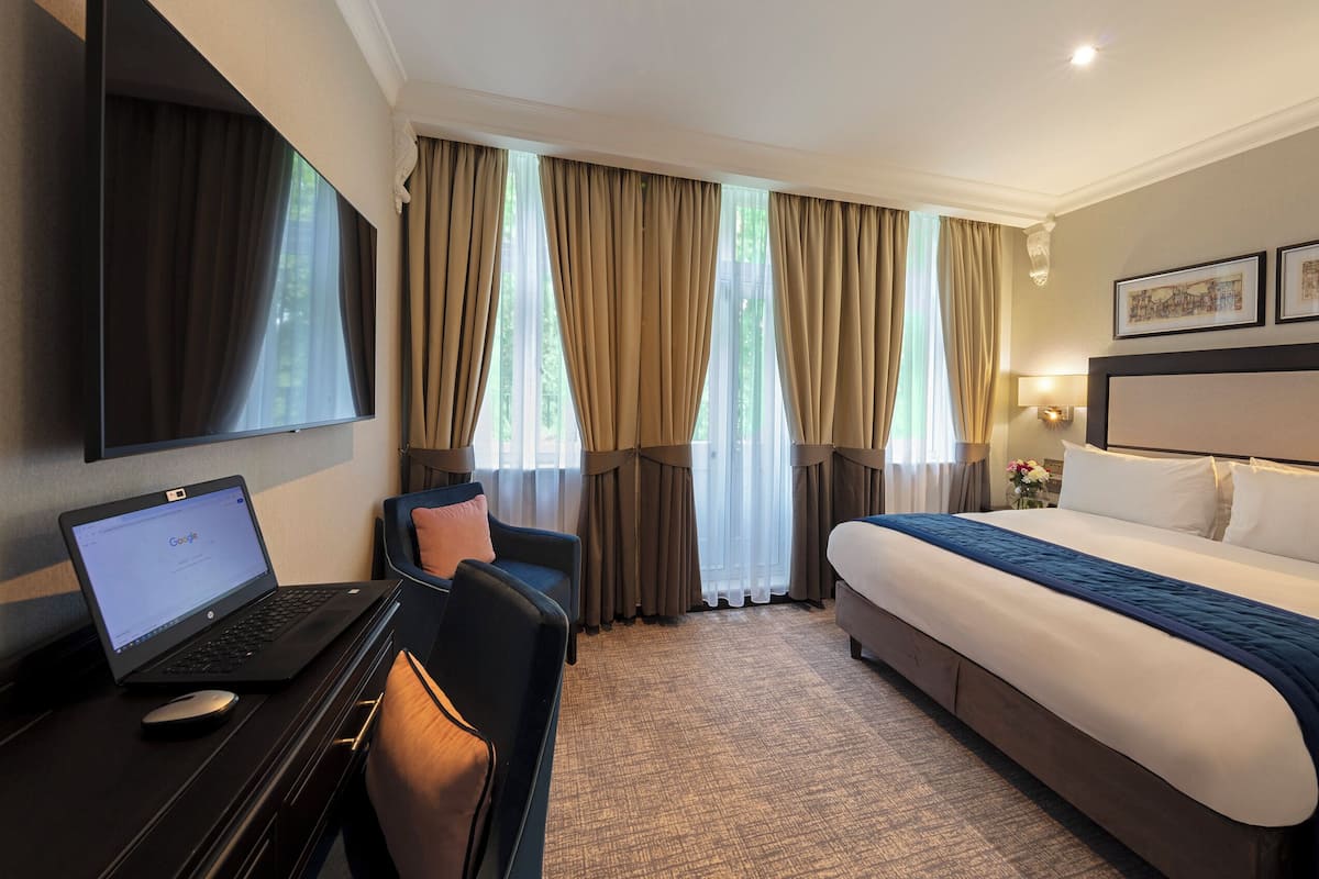 Una habitación de hotel con una cama, un escritorio con una computadora portátil, una silla y un televisor en la pared.