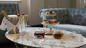 A marble table with a champagne bottle, glasses, a tiered dessert stand, and tea service. - Wellington Hotel by Blue Orchid (London)