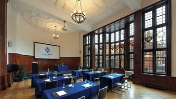 A conference room with multiple tables, a projector screen, and large windows with stained glass.