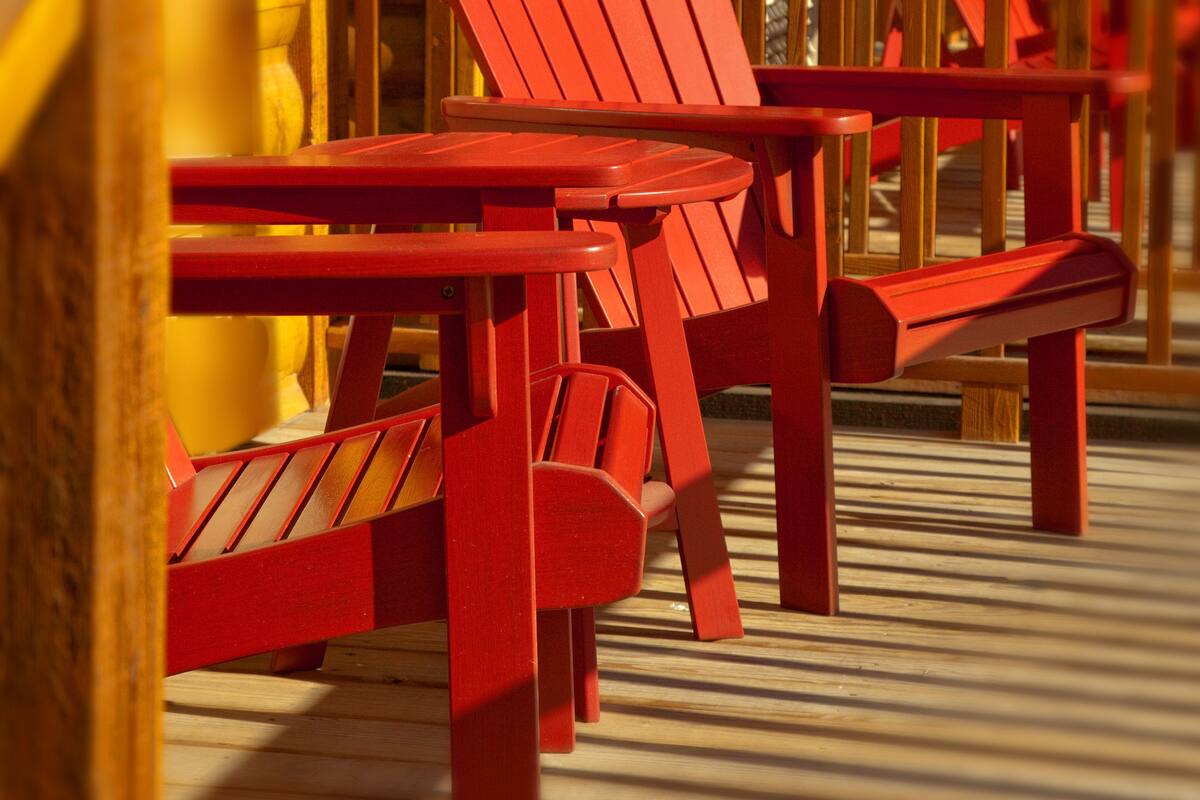 Une rangée de chaises Adirondack rouges et une table en bois sur une terrasse en bois.