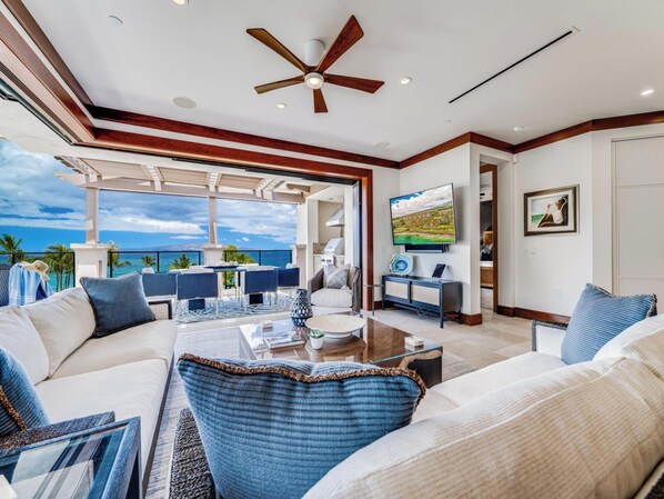 A spacious living area with a view of the ocean, a ceiling fan, and a television on a console table. - Wailea Beach Villas (Kihei)