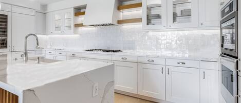 Une cuisine moderne avec des meubles blancs, un îlot en marbre et des appareils électroménagers intégrés.