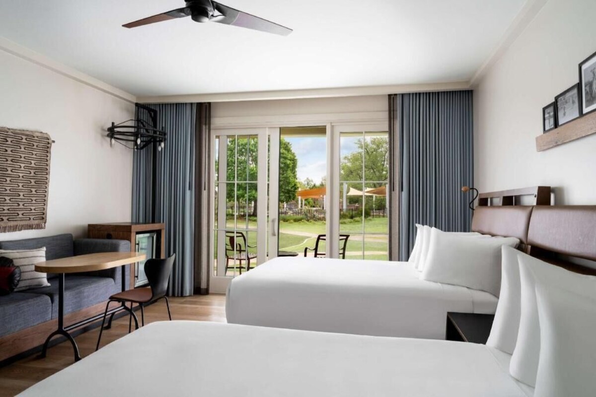 A hotel room with a bed, a desk, a chair, a ceiling fan, and a view of the outdoors.