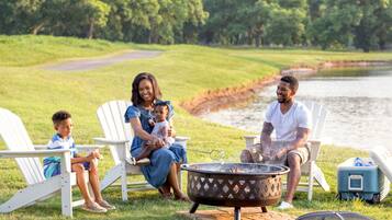 A family of three sitting on lawn chairs by a fire pit with a lake in the background.