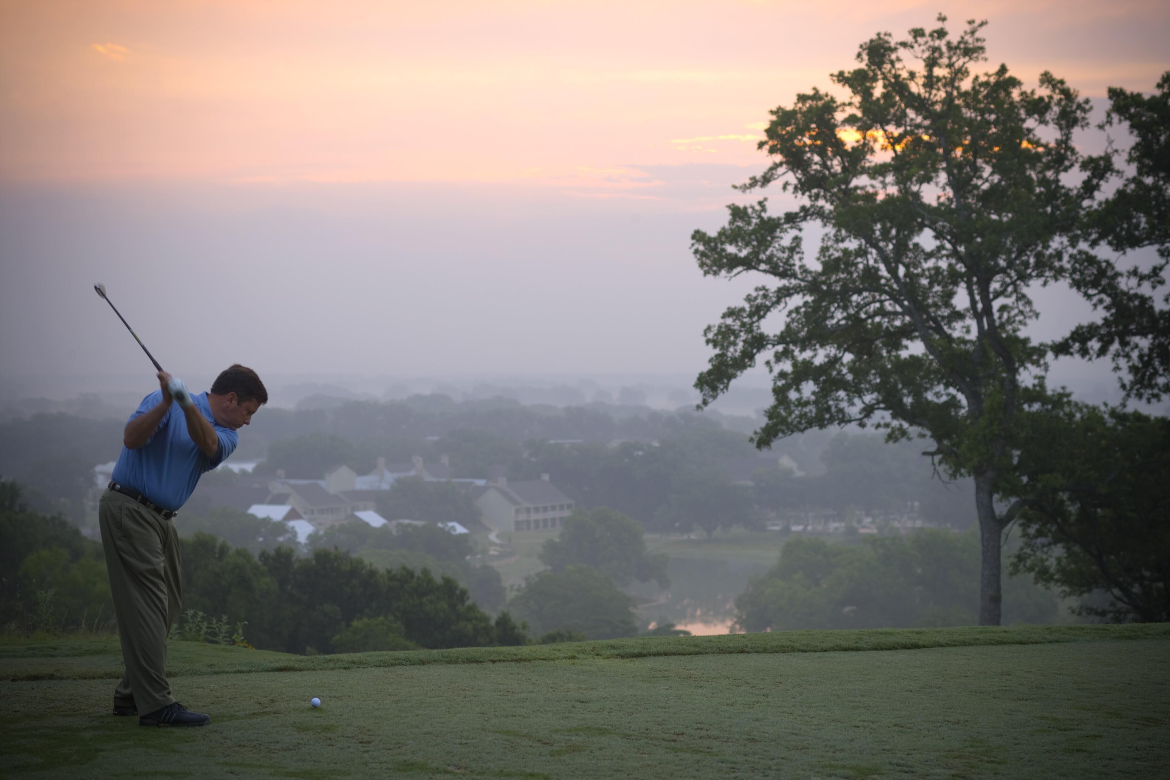 A golf course with a player in a blue shirt and khaki pants preparing to hit a ball.