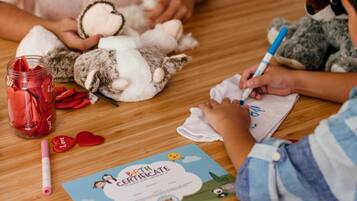 A child drawing on a birth certificate at a wooden table with stuffed animals and a jar of strawberries.