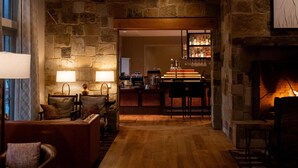 Uma sala de estar espaçosa com parede de pedra, piso de madeira, lareira e um espaço bar.