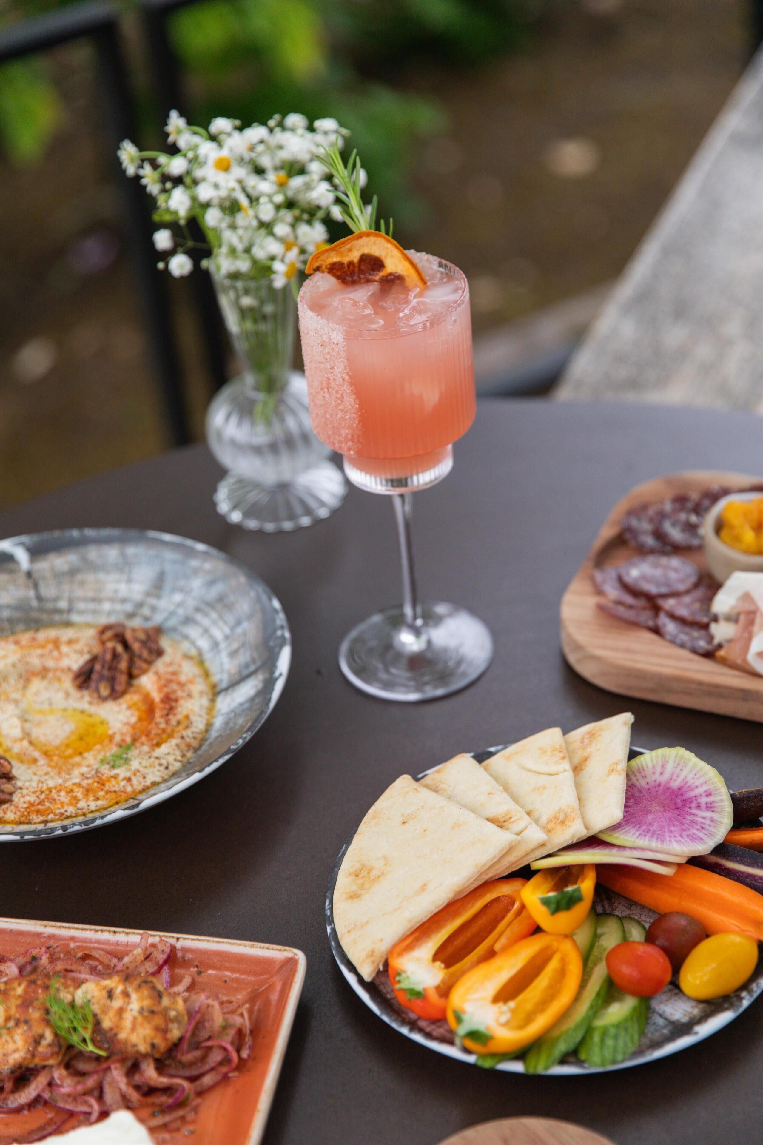 Une table dressée avec différents plats, notamment un verre d’une boisson rose, une assiette de galettes et un saladier de salade.