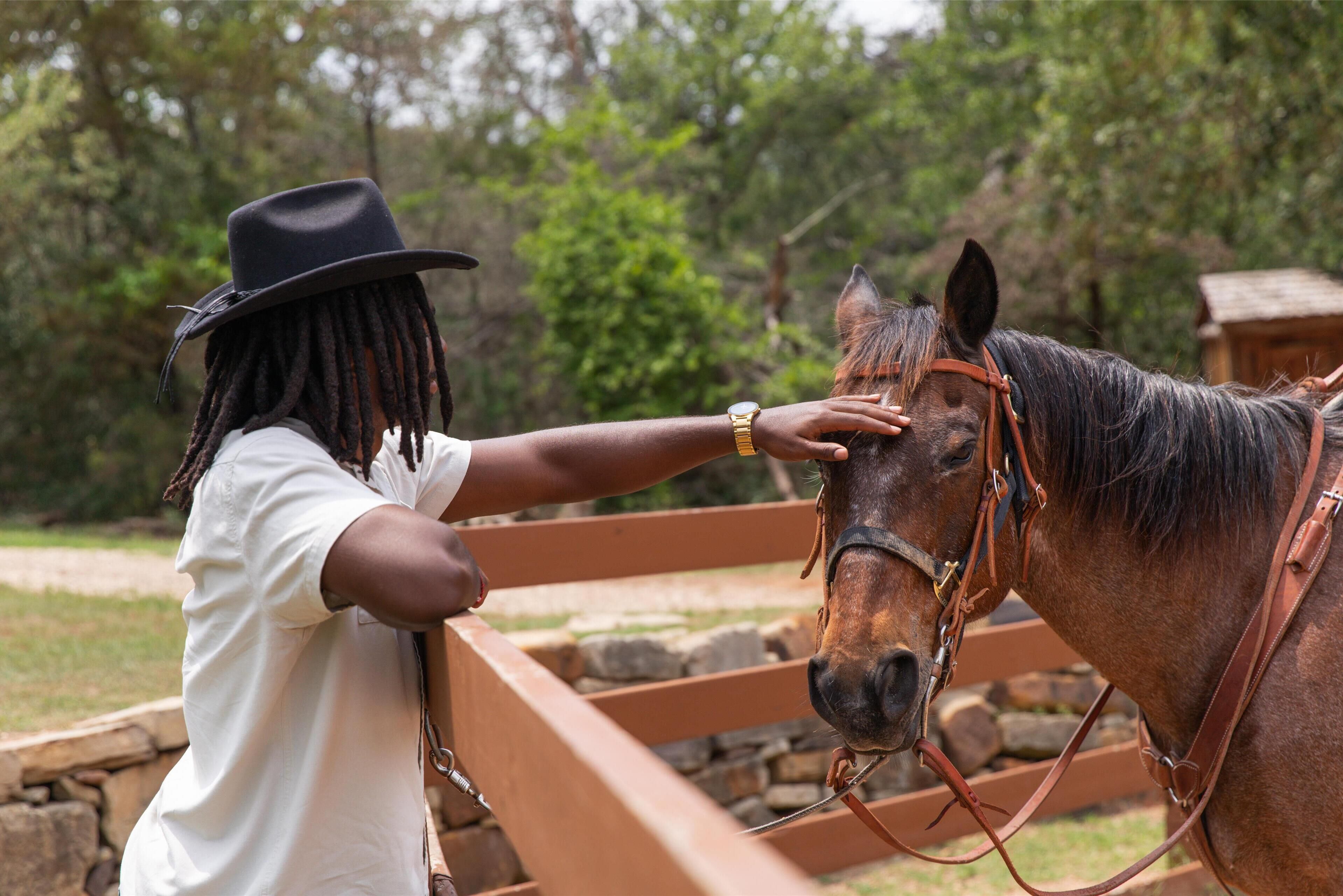 A person in a white shirt and black hat petting a horse.